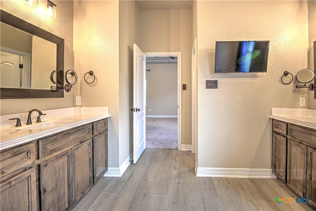 bathroom with wood finished floors, two vanities, baseboards, and a sink