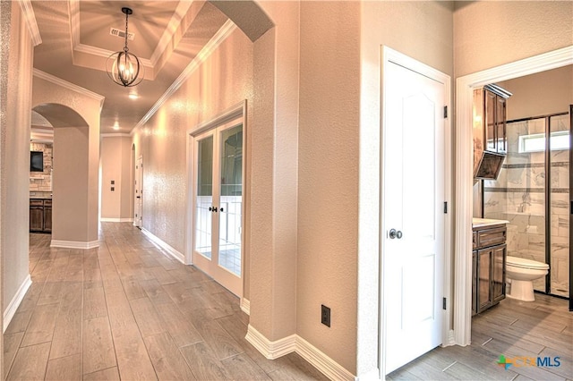 hall with wood finished floors, ornamental molding, a textured wall, arched walkways, and a raised ceiling