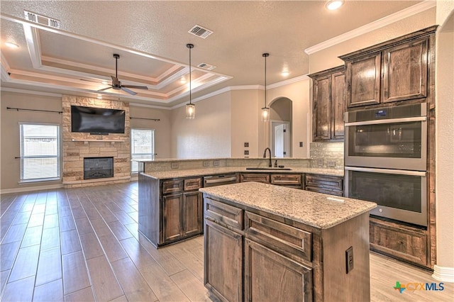 kitchen with visible vents, ceiling fan, double oven, a tray ceiling, and a fireplace