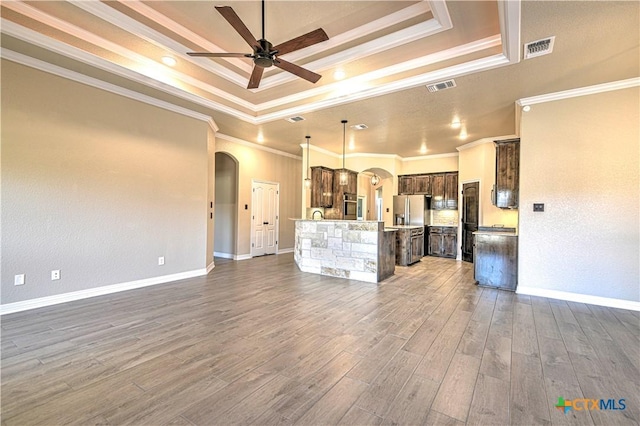 unfurnished living room with visible vents, a tray ceiling, wood finished floors, arched walkways, and ceiling fan