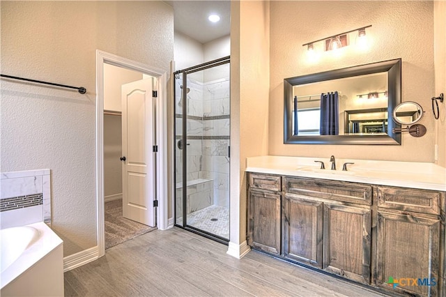 full bathroom featuring wood finished floors, a shower stall, a bath, vanity, and a textured wall