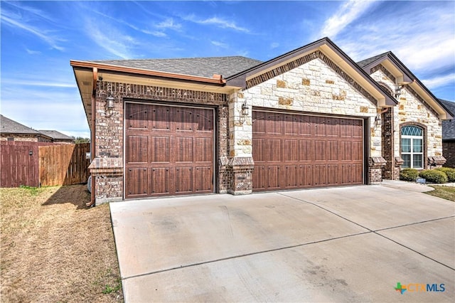 view of front of home with stone siding, driveway, a garage, and fence