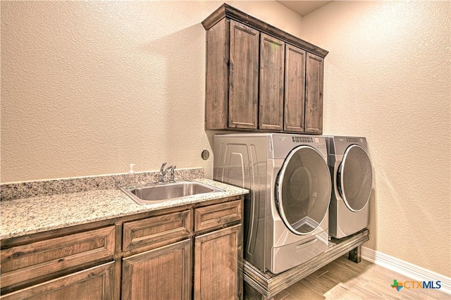 laundry room with cabinet space, a sink, light wood-style floors, a textured wall, and washer and clothes dryer