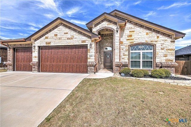 french country home with stone siding, an attached garage, concrete driveway, and a front yard