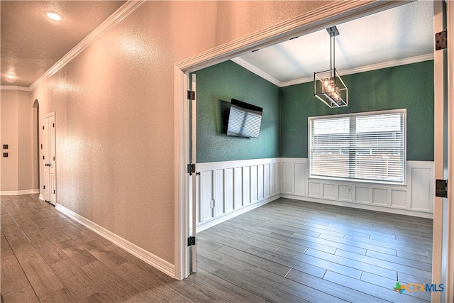 corridor featuring crown molding, dark wood-style floors, a textured wall, and wainscoting