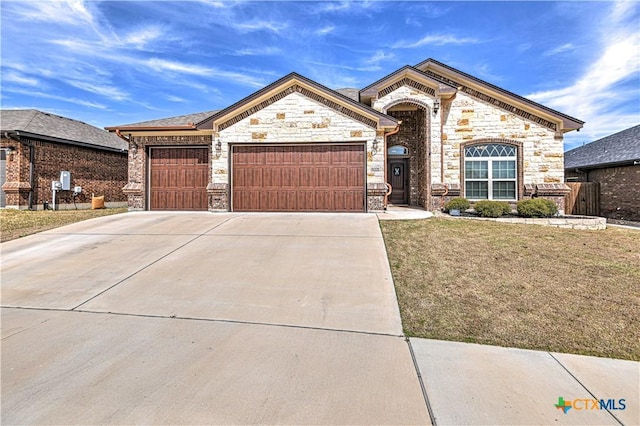 french country inspired facade with a front lawn, an attached garage, stone siding, and driveway