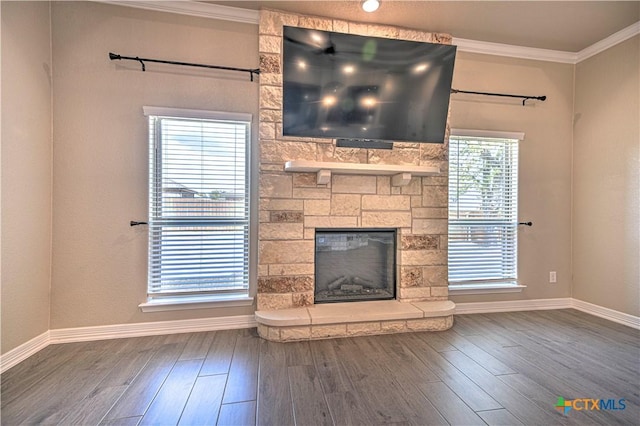 unfurnished living room with a stone fireplace, crown molding, wood finished floors, and baseboards