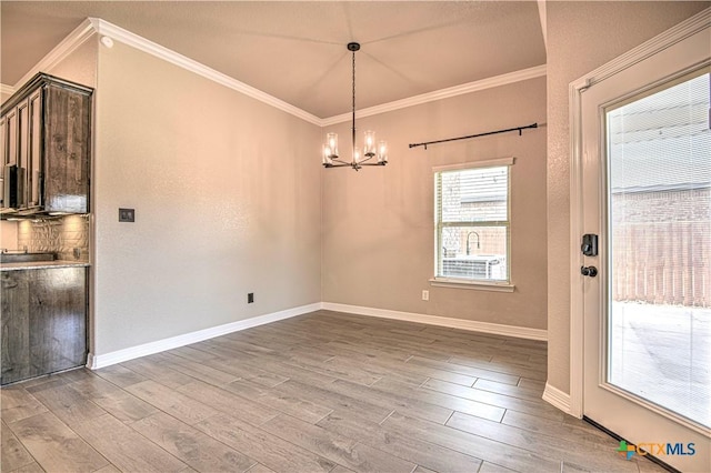 unfurnished dining area with an inviting chandelier, crown molding, wood finished floors, and baseboards