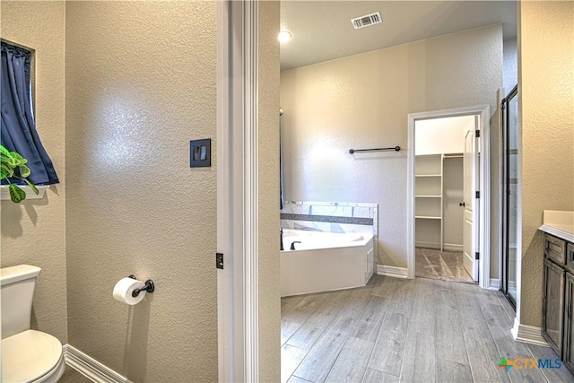 bathroom featuring wood finished floors, visible vents, toilet, a bath, and a textured wall