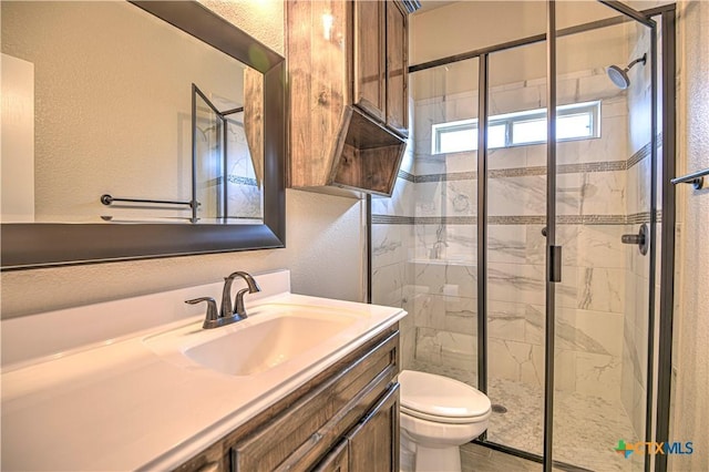 full bath with vanity, a shower stall, toilet, and a textured wall