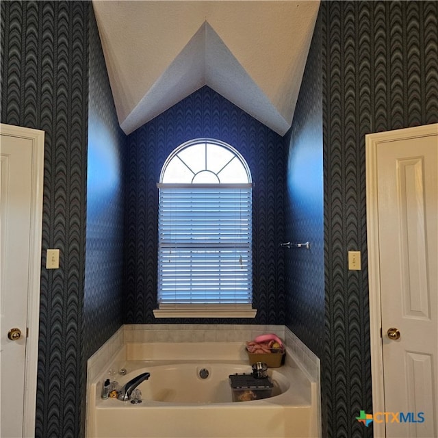 bathroom with a textured ceiling, a bathing tub, and vaulted ceiling