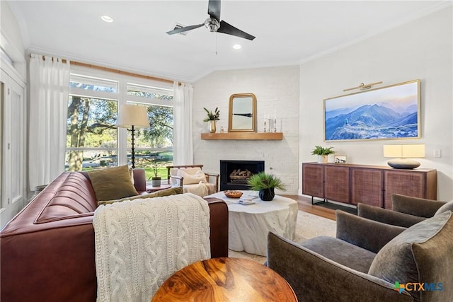 living room with hardwood / wood-style flooring, ceiling fan, ornamental molding, a brick fireplace, and vaulted ceiling