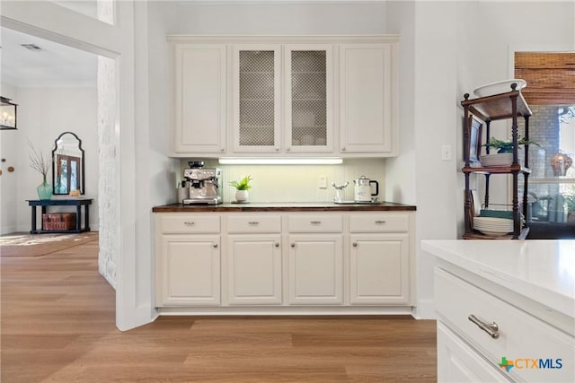 bar featuring ornamental molding, light hardwood / wood-style floors, and white cabinets