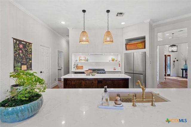 kitchen with pendant lighting, wood-type flooring, stainless steel fridge, ornamental molding, and a center island