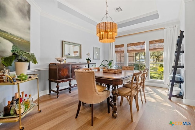 dining space with crown molding, a tray ceiling, and light hardwood / wood-style flooring