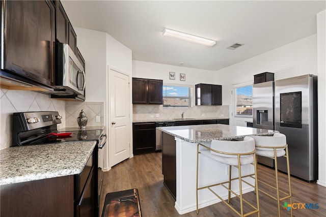 kitchen featuring light stone countertops, appliances with stainless steel finishes, a center island, and dark hardwood / wood-style flooring