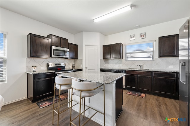 kitchen with a kitchen island, appliances with stainless steel finishes, dark hardwood / wood-style flooring, light stone countertops, and a breakfast bar area