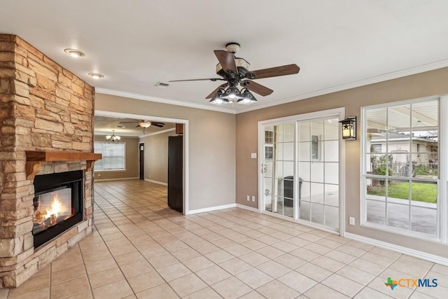 unfurnished living room with ceiling fan with notable chandelier, a stone fireplace, ornamental molding, and light tile patterned flooring