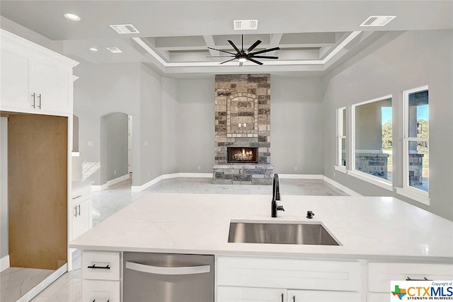 kitchen with sink, light stone countertops, ceiling fan, a stone fireplace, and dishwasher