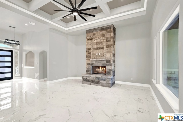 unfurnished living room with coffered ceiling, ceiling fan, beam ceiling, a fireplace, and a high ceiling