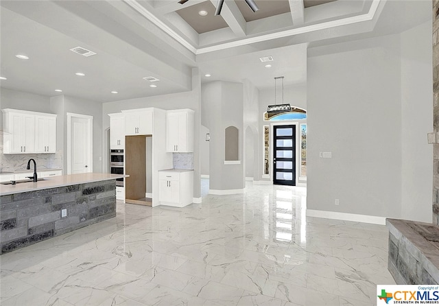 kitchen featuring white cabinetry, sink, tasteful backsplash, beam ceiling, and stainless steel double oven