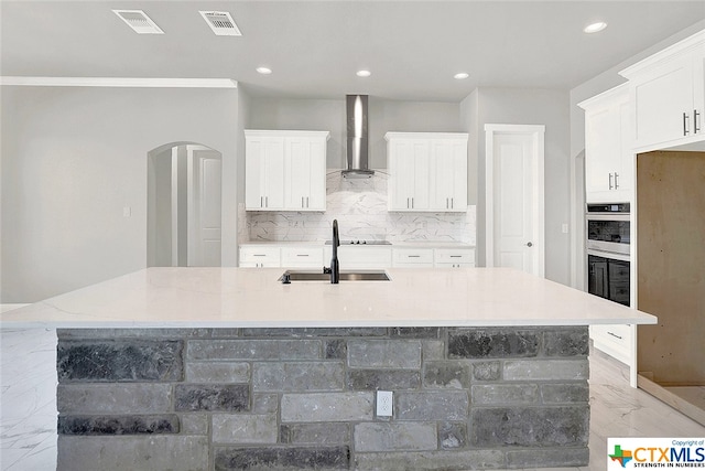 kitchen with a large island with sink, light stone countertops, wall chimney exhaust hood, and white cabinets