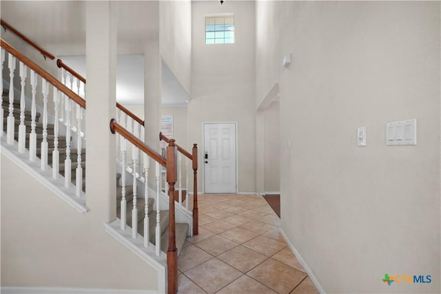 foyer featuring stairs, light tile patterned flooring, baseboards, and a towering ceiling