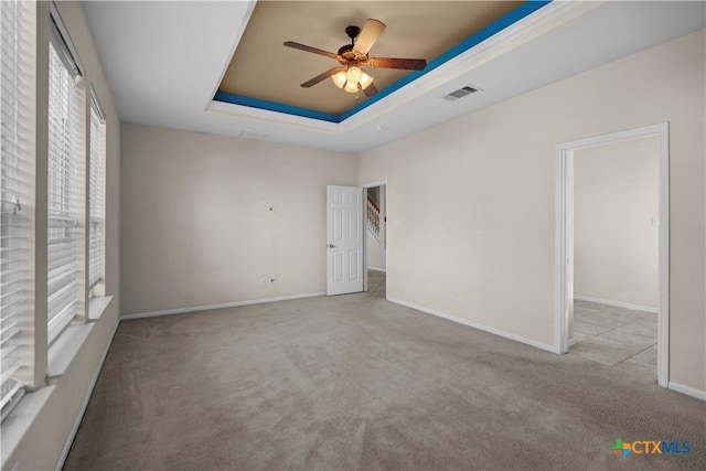 spare room with visible vents, a ceiling fan, a tray ceiling, carpet floors, and baseboards