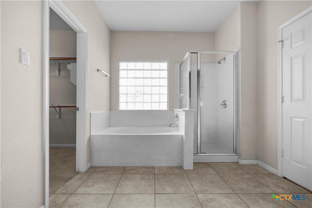 bathroom featuring tile patterned flooring, a stall shower, a spacious closet, and a garden tub