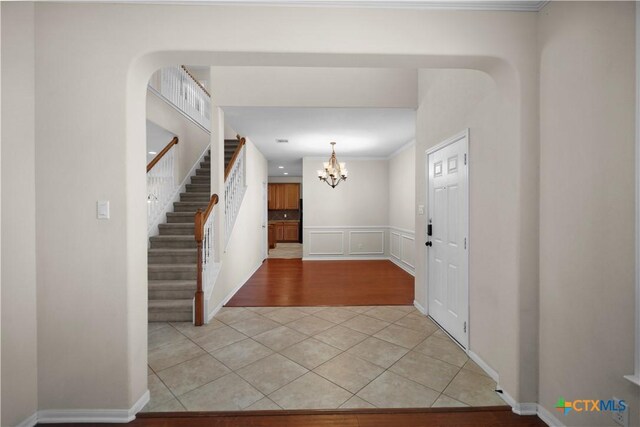 foyer featuring arched walkways, a decorative wall, light tile patterned floors, a chandelier, and stairs