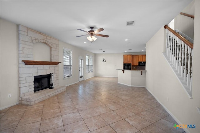 unfurnished living room featuring visible vents, a fireplace, light tile patterned floors, ceiling fan, and stairs