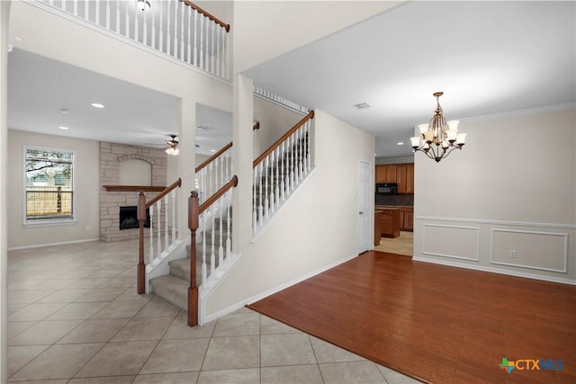 stairs featuring visible vents, a fireplace, tile patterned floors, a decorative wall, and ceiling fan with notable chandelier