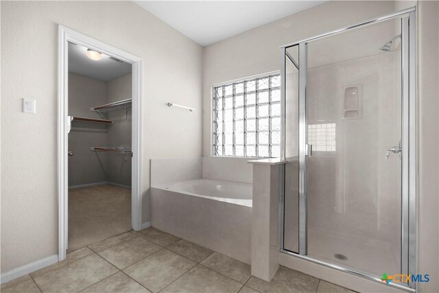 bathroom with tile patterned floors, a walk in closet, a garden tub, and a stall shower