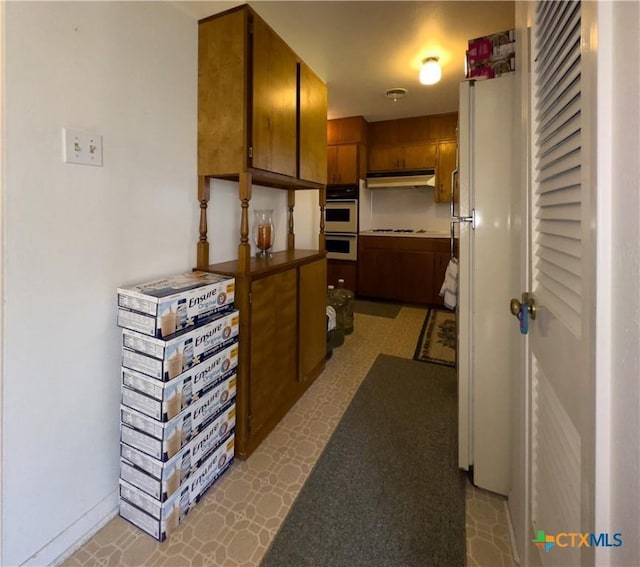 kitchen featuring brown cabinets, under cabinet range hood, stovetop, double oven, and baseboards