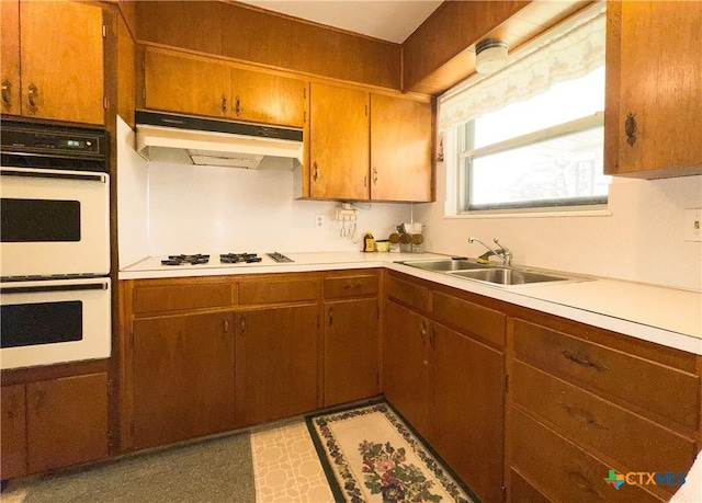 kitchen featuring white appliances, light countertops, under cabinet range hood, and a sink