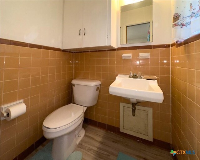 bathroom with wood finished floors, a wainscoted wall, a sink, tile walls, and toilet