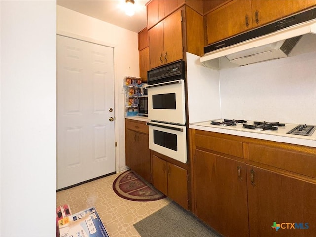 kitchen with white appliances, brown cabinetry, light floors, light countertops, and under cabinet range hood