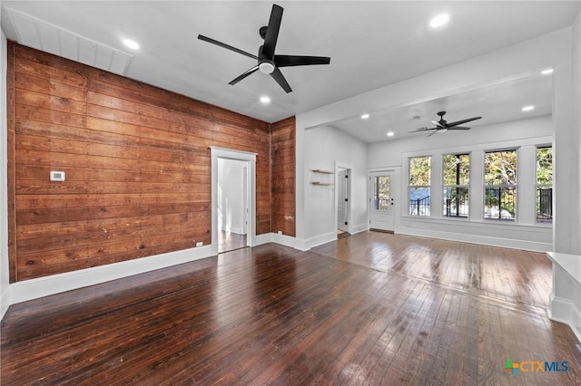 unfurnished living room with wooden walls, ceiling fan, and dark wood-type flooring