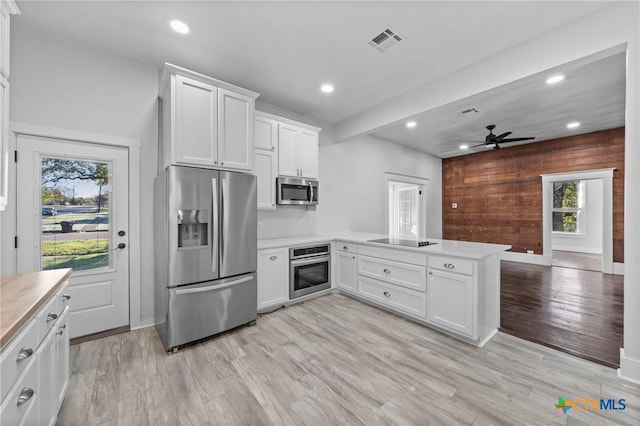 kitchen featuring white cabinets, kitchen peninsula, stainless steel appliances, and wooden walls