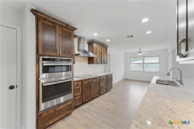 6022 Wildwind Dr, Windcrest, TX 78239 - kitchen featuring wall chimney exhaust hood, a sink, stainless steel double oven, light wood finished floors, and backsplash