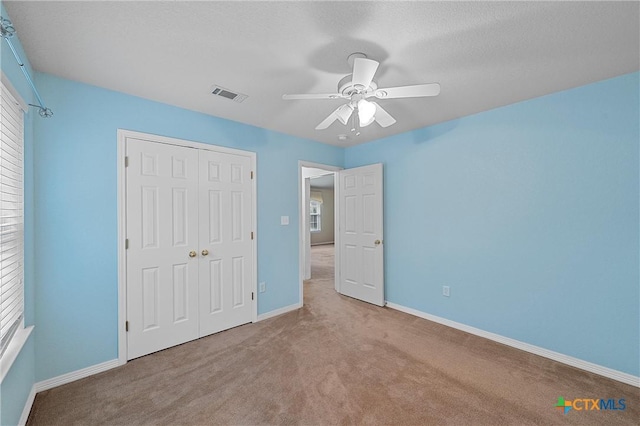 unfurnished bedroom featuring light carpet, a textured ceiling, a closet, and ceiling fan