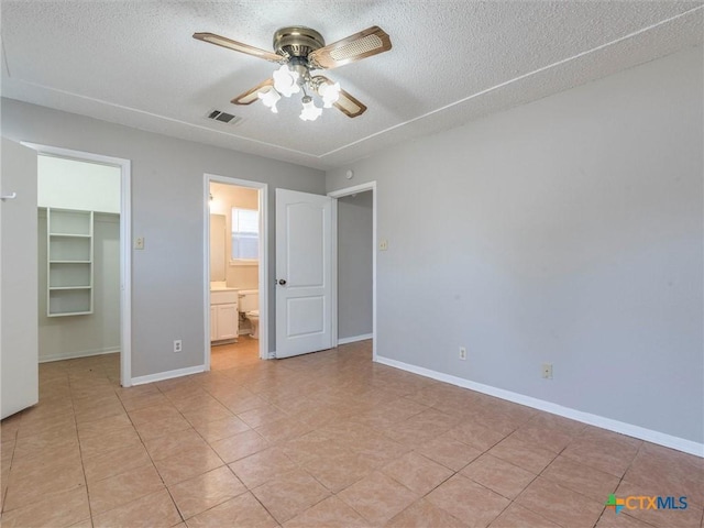 unfurnished bedroom featuring ceiling fan, a spacious closet, a textured ceiling, and a closet