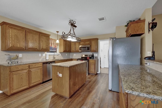 kitchen with appliances with stainless steel finishes, decorative light fixtures, sink, a center island, and light hardwood / wood-style floors