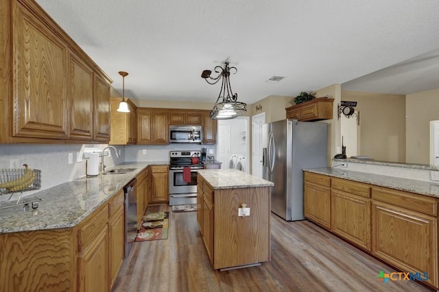 kitchen with stainless steel appliances, a center island, hanging light fixtures, and washer and dryer