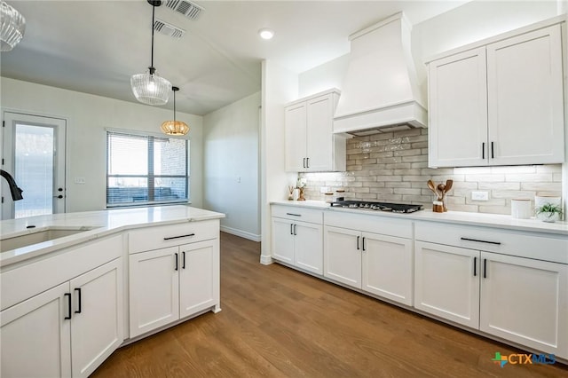 kitchen with decorative light fixtures, stainless steel gas stovetop, sink, white cabinets, and custom exhaust hood