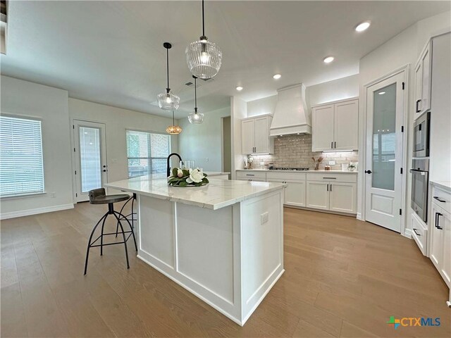 4316 Sunflower Ln, Temple, TX 76502 - kitchen with premium range hood, appliances with stainless steel finishes, a large island with sink, decorative backsplash, and light wood-style flooring