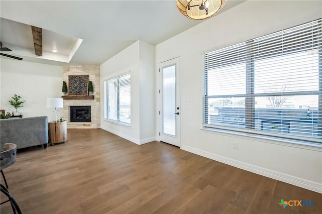 living room with a tray ceiling, a stone fireplace, wood-type flooring, and ceiling fan