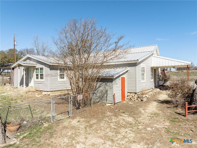 back of house with a gate, dirt driveway, fence, and metal roof