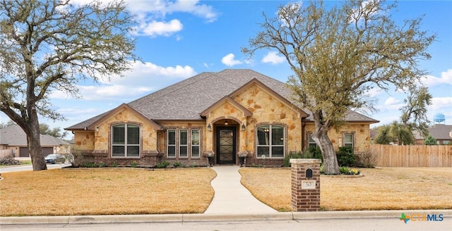 french provincial home featuring a front lawn, fence, brick siding, and stone siding