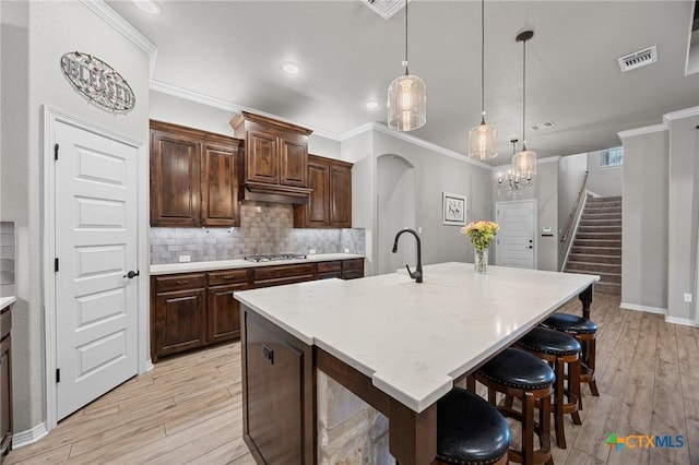 kitchen featuring visible vents, backsplash, light countertops, ornamental molding, and light wood-style floors